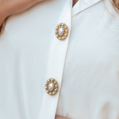 Capas de botões douradas com pérola ao centro e contorno de pérolas, numa camisa branca